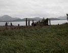 Low clouds over a bay, with mountains in the distance and deteriorated wooden pilings on the shore.