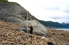 A man stands by a very large rock deposited by a landslide.
