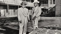 A.G. Gaston and R.A. Hester, wearing suits, ties, and hats, in the courtyard of Gaston Motel