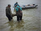two people carrying a fossil through shallow water to a small boat