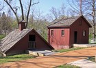 Photo of two rust-red historic farm outbuildings, an ice house and a chicken house