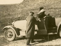 Black and white photograph of woman seated in luxury car with man standing by door
