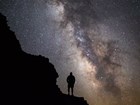 The dark silhouette of a person standing on a rocky slope, in front of a bright starry sky.