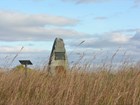 A stone grave monument, stands in a field of tall grass.