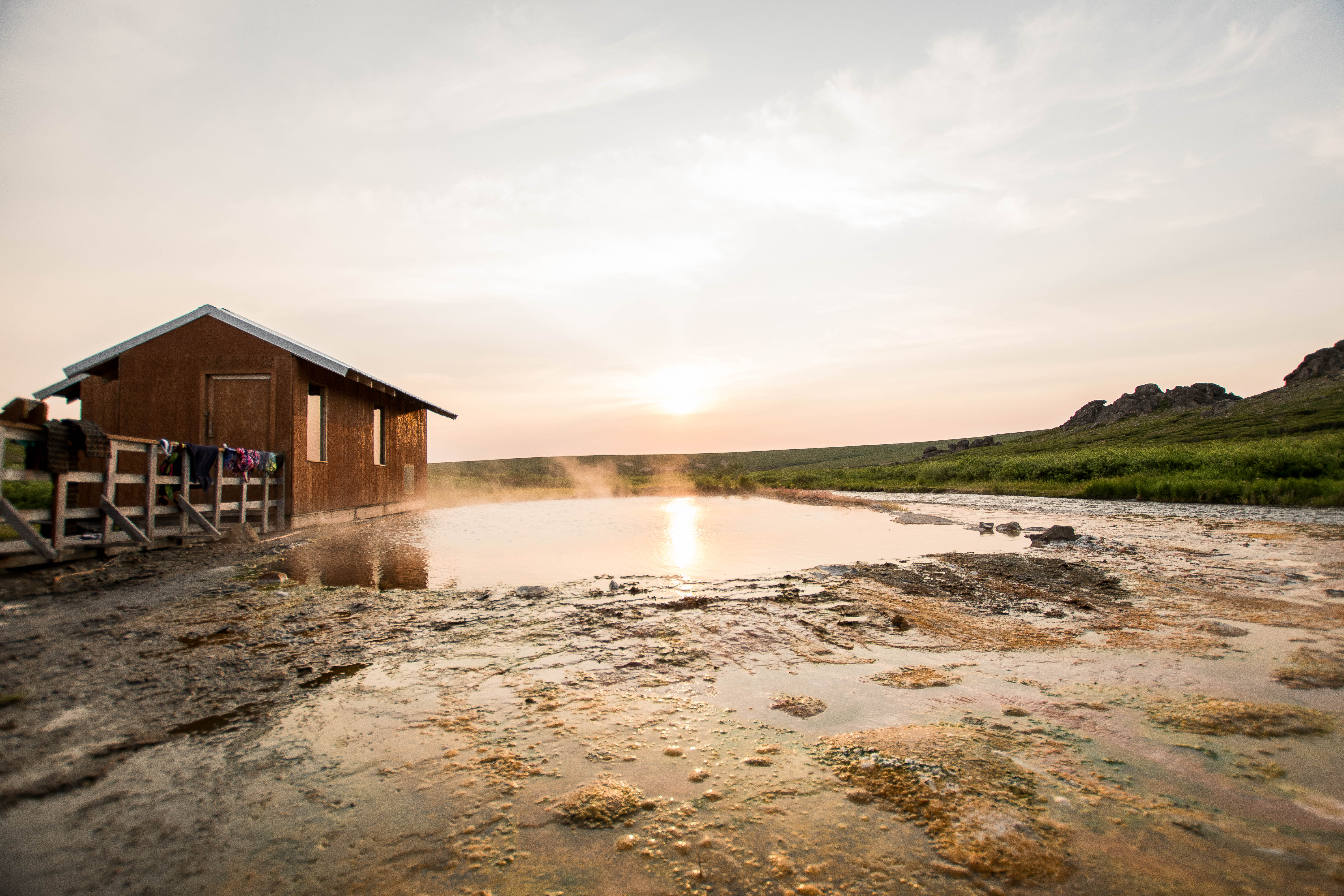 Steam rises from a shallow pool near an enclosed bathouse.