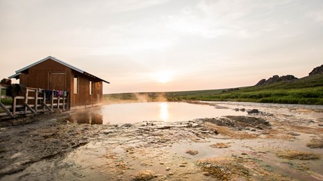Steam rises from a shallow pool near an enclosed bathouse.