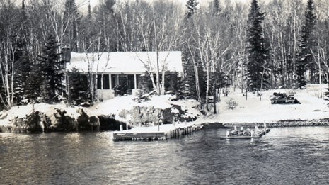 cabin covered by snow, dock damage in the foreground after a late-season storm