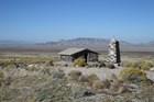 A stone building sits in a vast desert landscape with distant mountains.