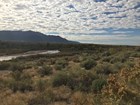 Desert shrubs leads to a distant shallow creek and distant mountains.