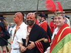 Three men stand in elaborate clothing with feathers and paint adorning their heads