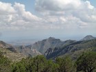 View from a mountaintop of trees, mountains, and a valley in the distance with cloud cover.