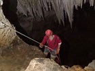 a helmeted person on a climbing rope descending a into dark passage way