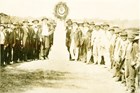 Sepia toned photograph of a group of men surrounding an obelisk shaped monument.