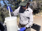 A scientist filling a water bottle from a larger container of water.