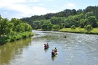 Three canoes on a river with green banks and a blue sky.