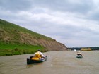 Two canoers on shallow waters with grey sky behind.