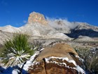 A dusting of snow on the Guadalupe Mountains and plants and rocks in the foreground.