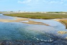water enters a salt marsh with dunes and a lighthouse in the background