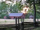behind a wooden fence stands an old weathered red barn in a field at sunset.