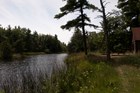 A log cabin to the right of a pond, which is surrounded by trees and grasses