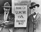 Two men in suits and hats standing next to a sign that reads Home of U.M.W. of A. District No. 17.