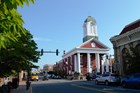 Red brick building with a white columnated portico and a clocktower sits on a street corner.