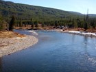 Bright blue water in a bending river lined by evergreen trees and a tree-covered hill.