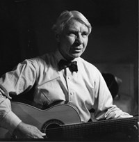 black and white image of Carl Sandburg sitting, playing a guitar