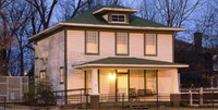 White two-story building with green trim lit at dusk with trees behind.
