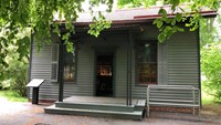 Leaves of overhanging trees frame a one-story structure with siding and a small front porch.