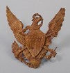 A yellow metal Army helmet insignia of an eagle with a shield.