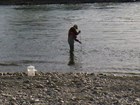 A person standing in a river holding a bottle on a pole under water to collect river samples