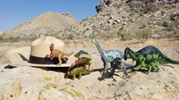 Dinosaur models sit on a rock with a ranger hat