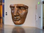 Bronze sculptures of torch and woman's face in museum gallery