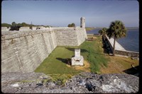 A furnace in an area of turf between the masonry wall of a fort and a seawall alongside water.