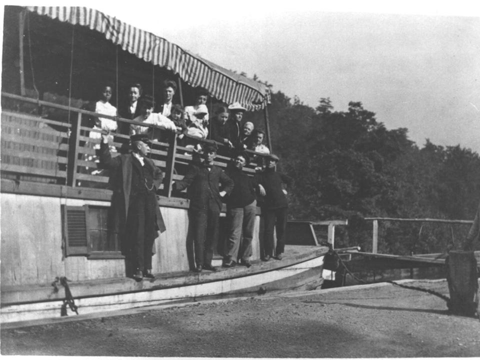 Historical black and white photo of men, women, and children aboard a canal boat.