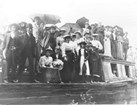 Historical black and white photo of men, women, and children gathered on a canal boat.