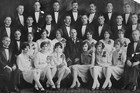 A group of men and women in tuxedos and gowns for a formal portrait.