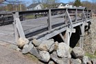 Wooden bridge extends from grassy field to stone chimney.