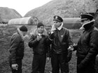 Four men in winter gear eating apples in front of round buildings. 