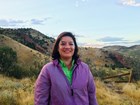 Woman wearing purple jacket smiles on hillside