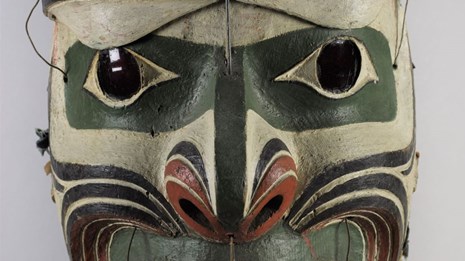 Painted mask of tan, brown, and red bands, green around the eyes, brown eyebrows and, a red mouth.