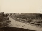 An 1885 photo shows a improved dirt road flanked by wood fences and farms.