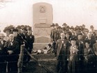 Well-dressed men and women pose in front of a stone war memorial in a 1907 photo.