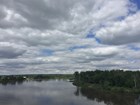 River bend and cloudy blue sky. River lined with green trees.
