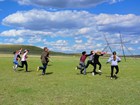 A group of teenagers run to the right holding sticks up in a game.