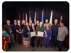 A group of 13 pose. Two hold large certificates. 