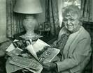 Black and white photo of older woman looking through newspapers and family photos.