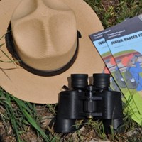 Ranger hat on grass with binoculars and booklets.