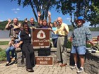 Group of people. Lewis and Clark Trail Logo sign reads Lewis and Clark Trail Auto Tour Route.